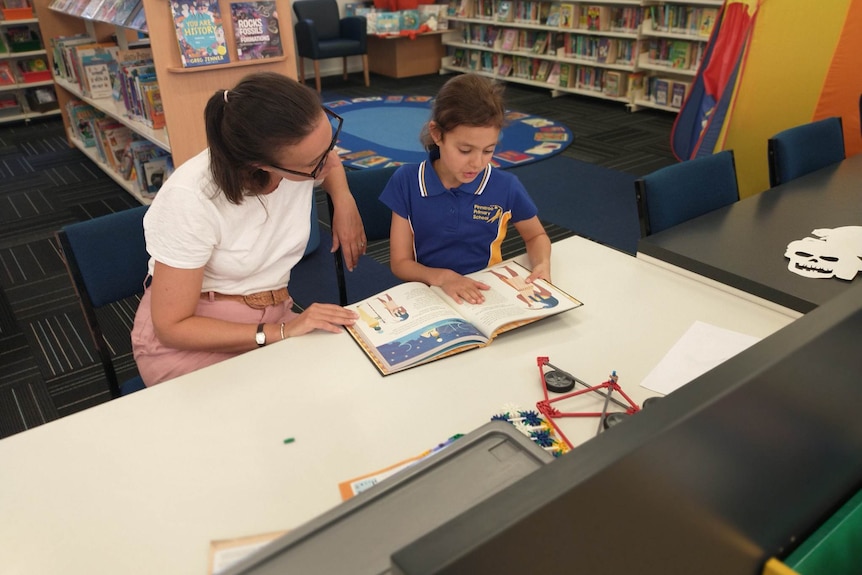 A teacher and a student sit at a table together in a library.