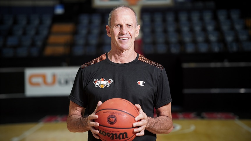 Brian Goorjian holds a basketball and smiles, inside the WIN Entertainment Centre.