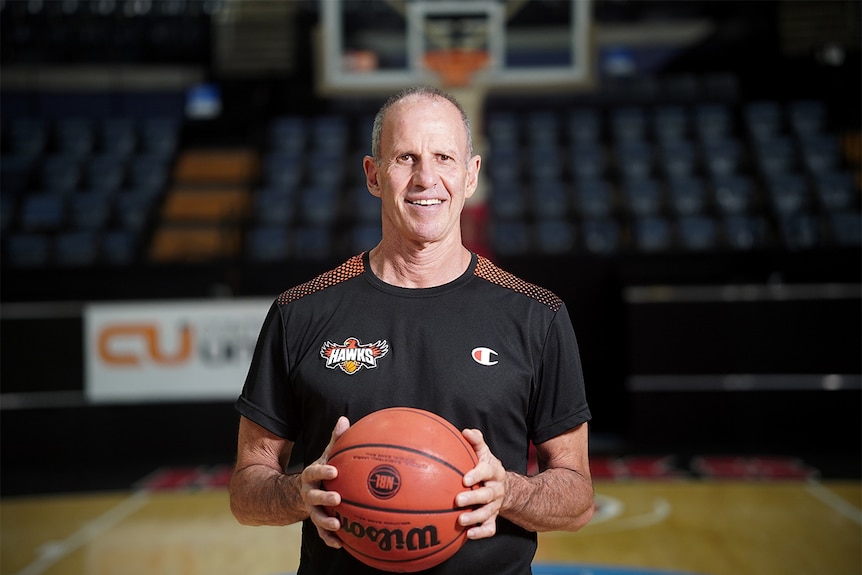 Brian Goorjian sostiene una pelota de baloncesto y sonríe, dentro del WIN Entertainment Center.