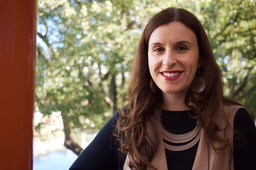 A portrait of Randa Abdel-Fattah smiling at the camera, with tree branches in the background.