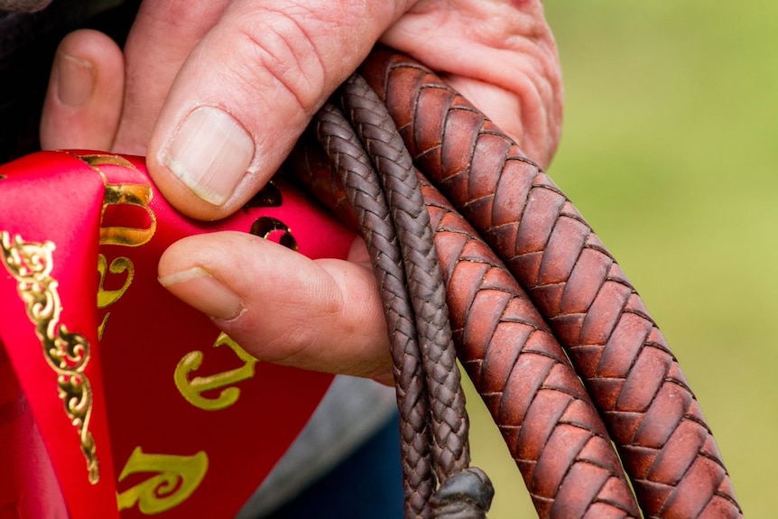 A close up picture of a man holing a plaited leather whip