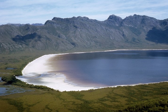 Wide shot of an inland lake with pink sand surrounded by a rocky mountain range