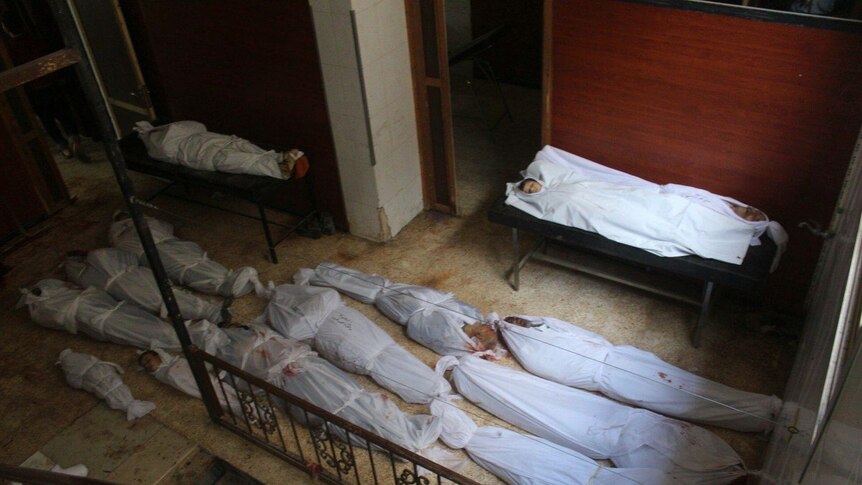 12 men, women and children in white shrouds on a floor, killed in the bombing of Ghouta by Syrian troops