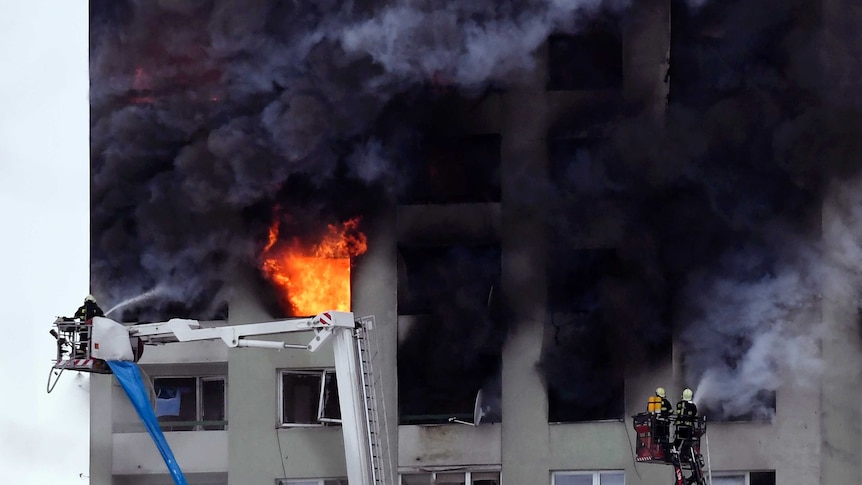 Firefighters on a ladder try to extinguish a fire in a 12-storey apartment block.