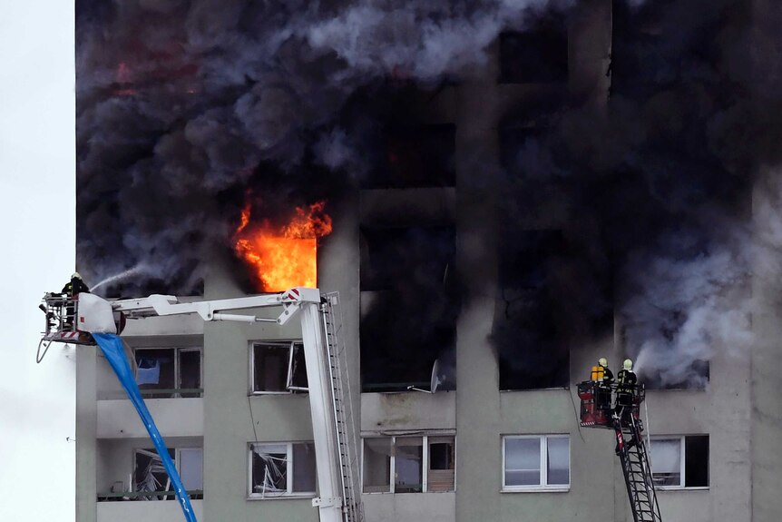 Firefighters on a ladder try to extinguish a fire in a 12-storey apartment block.