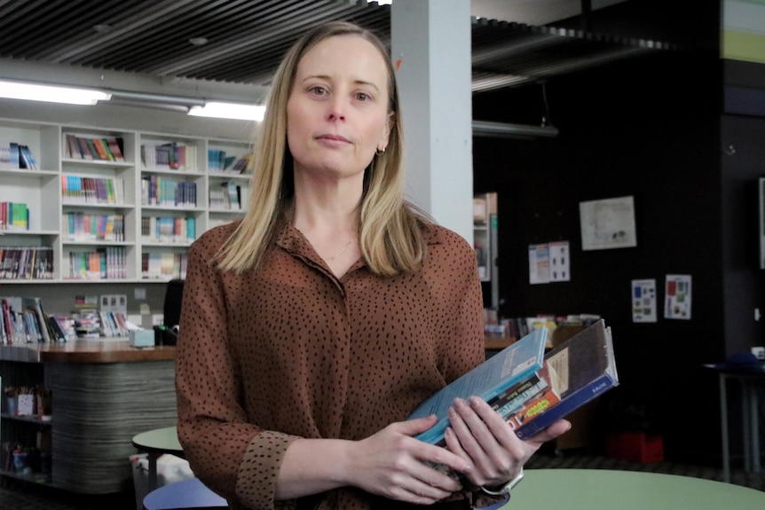 A woman wearing a brown shirt holds a stack of books.
