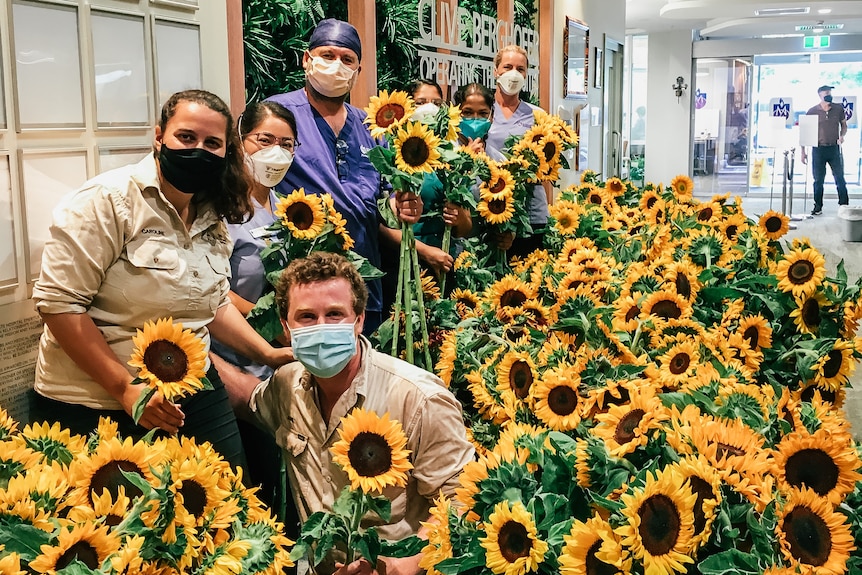 Two farmers and hospital staff pose with many sunflowers in a hospital
