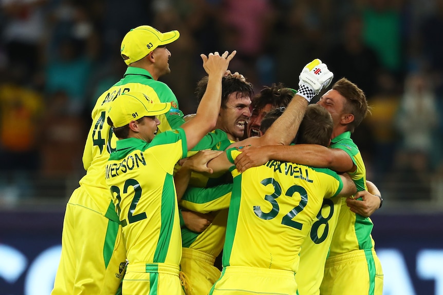 Cricket players wearing yellow in  a huddle celebrating winning a tournament