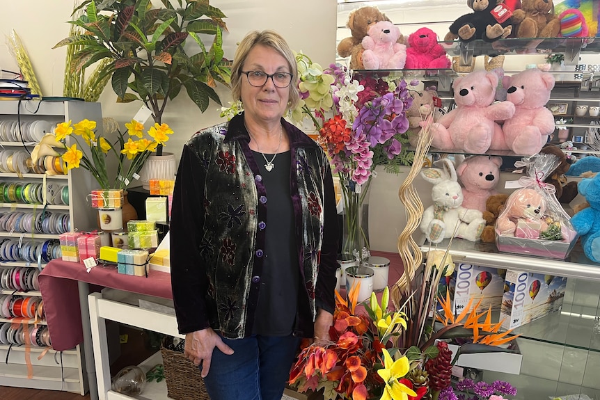 A woman stands in a shop full of bright flowers.