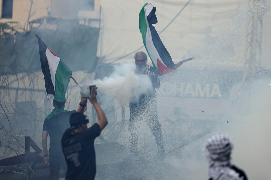 Four men are pictured, two of them waving a Palestinian flag, while protesting at the US embassy in Lebanon.