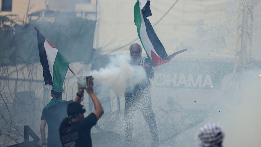 Four men are pictured, two of them waving a Palestinian flag, while protesting at the US embassy in Lebanon.