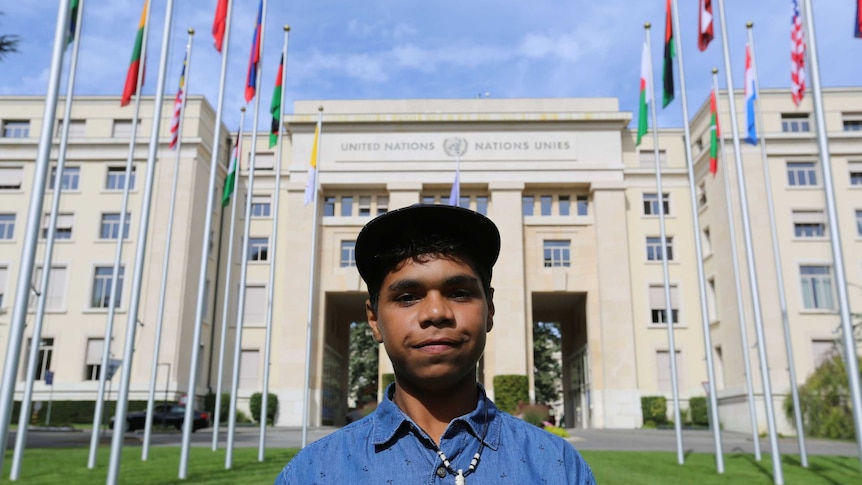 Dujuan Hoosan, a boy in a hat, stands looking proudly in front of the United Nations building in Geneva.