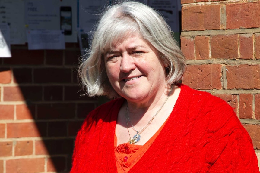 Julie Davis  stands outside the post office wearing a bright red top on a sunny day