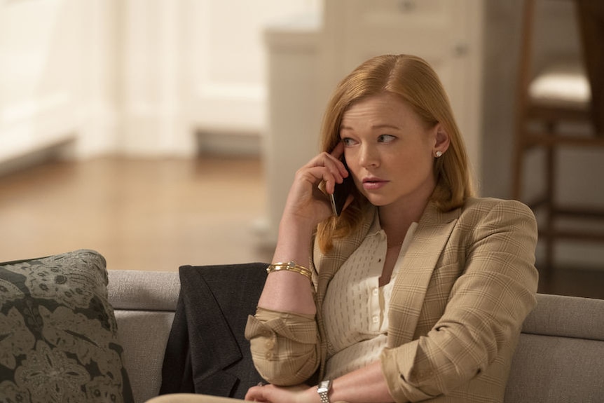 A red-haired woman sits, relaxed, on a couch while chatting on a mobile phone. Her eyes are looking away to her right.