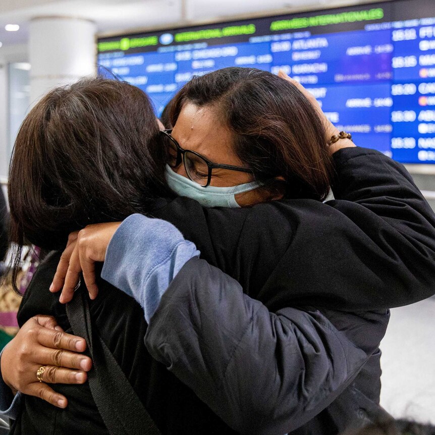Two people hugging each other in masks in an airport