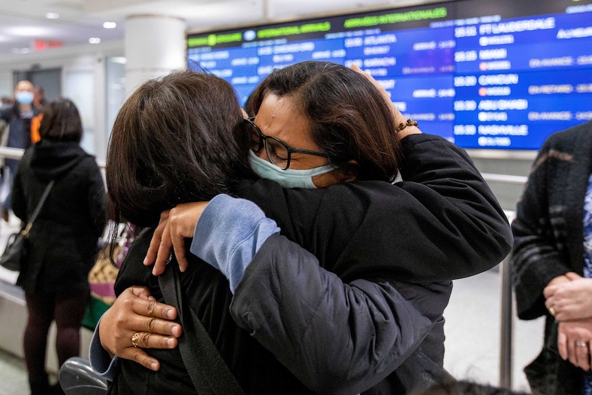 Two people hug each other in masks at an airport