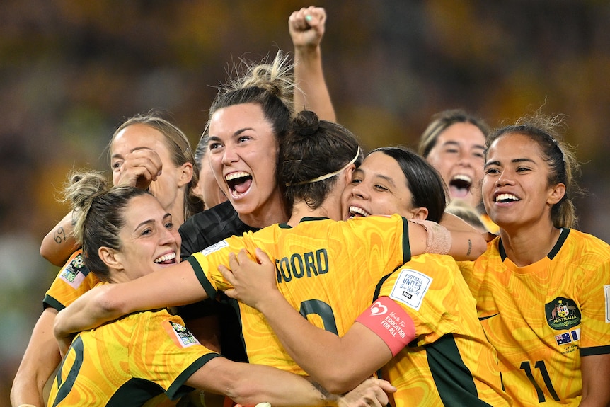 The Matildas hug, cheer and fist pump the air as they celebrate on the field.