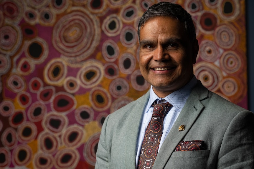 A man stands in front of an Aboriginal artwork.