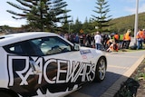 A black and white car with a big Racewars logo on its side parked near a group of people in Albany.