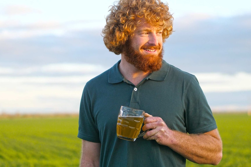 A man, wearing a green t-shirt, with a beer in his hand.