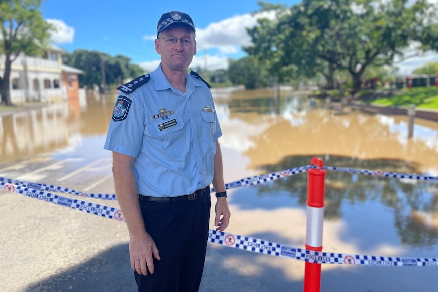 police officer stands in front of flood water and police tape