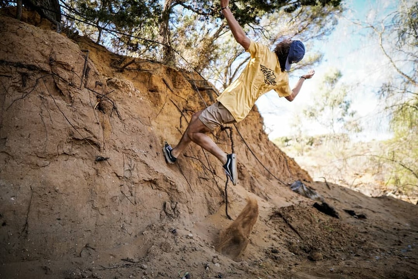 A young man about to doing a backwards somersault on a riverbed