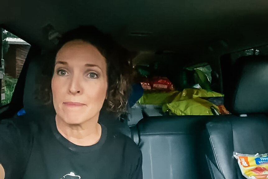 A selfie of a woman in a car with seats full of bags