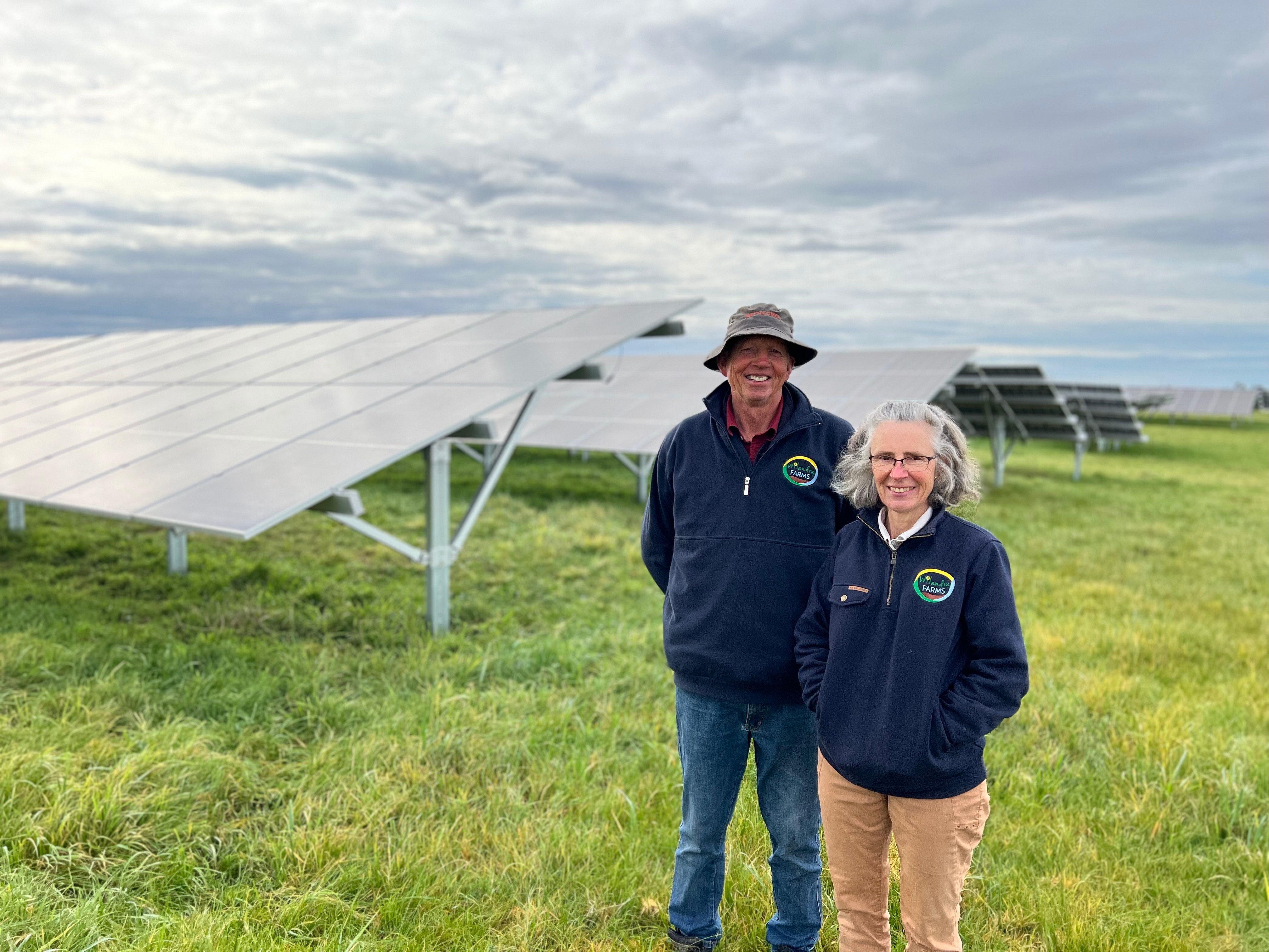 Wilco and Sandra stand side-by-side smiling with banks of solar panels in the background