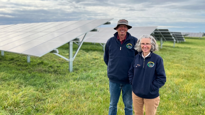 Wilco and Sandra stand side-by-side smiling with banks of solar panels in the background