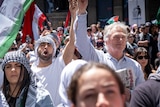 A crowd stands at Melbourne's State Library, many waving Palestinian flags, on a sunny day.