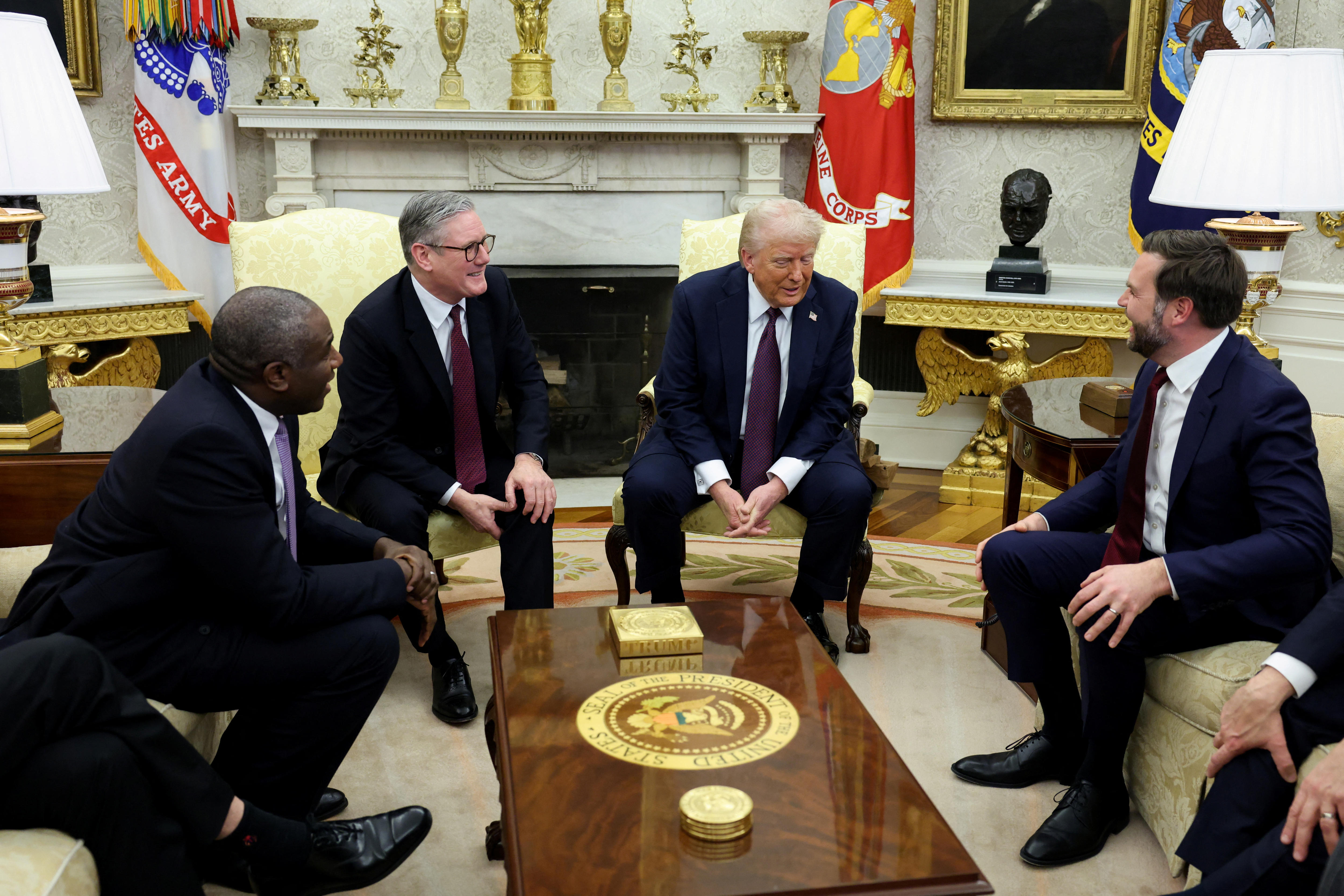 Four men sit on seats chatting and laughing with each other in an ornate office
