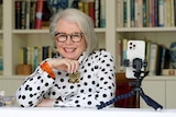 Older woman smiling with a phone on tripod and miniature studio lightening equipment in front of her