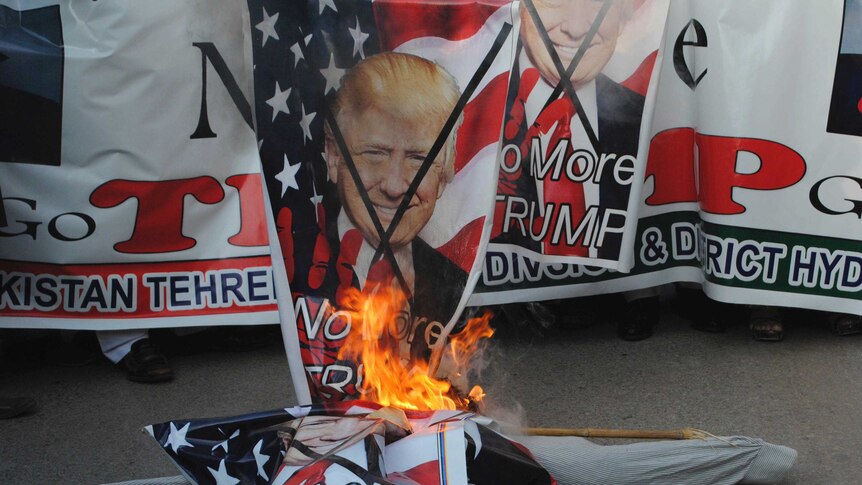 Protesters burn a poster of Donald Trump's face.