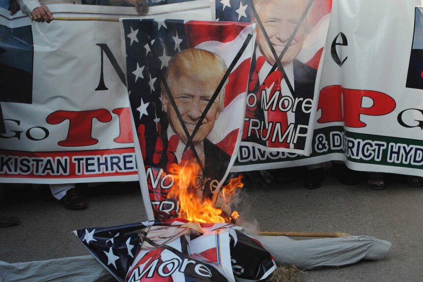 Protesters burn a poster of Donald Trump's face.