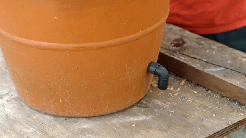 Elbow drainage pipe filled in the side of a plastic pot.