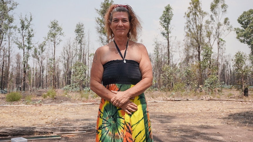 A woman in a colourful dress stands in front of burnt trees
