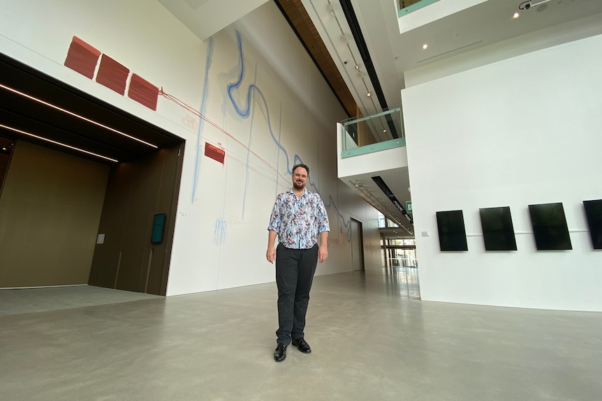 A wide angle shot of a man standing in a large open gallery space