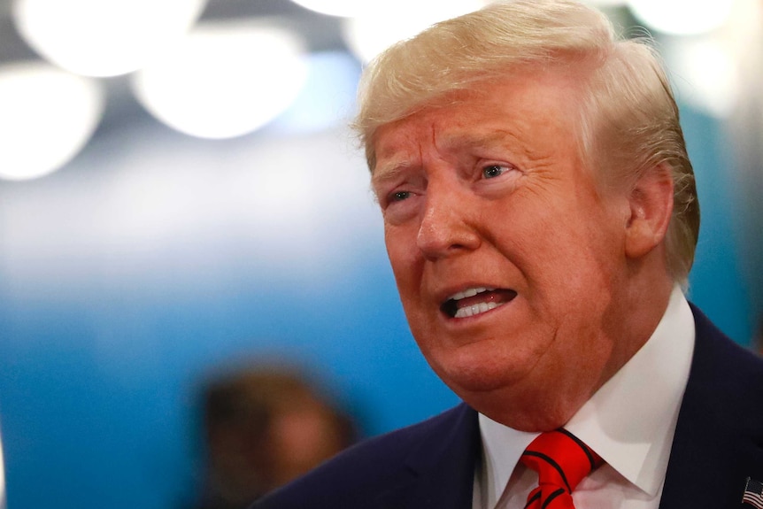 Donald Trump speaks in front of a blue background.