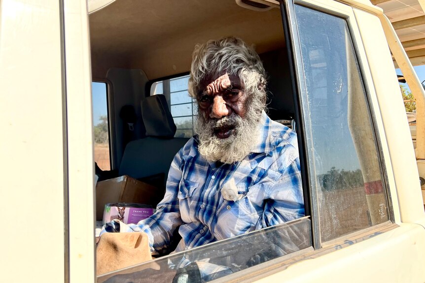An old man with a white beard gazes out of a car window