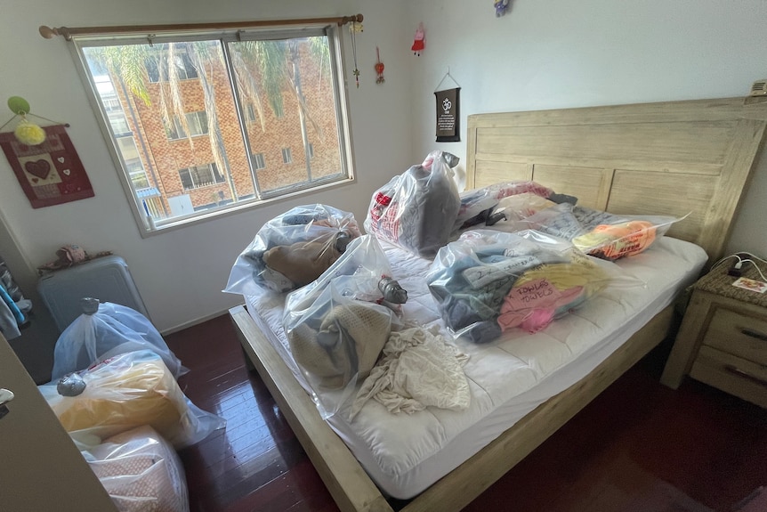 Plastic bags containing clothes sit on a large bed.