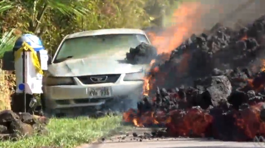 A mound of lava covered in a cracked black crust and taller than the car it is next to starts to destroy the vehicle.