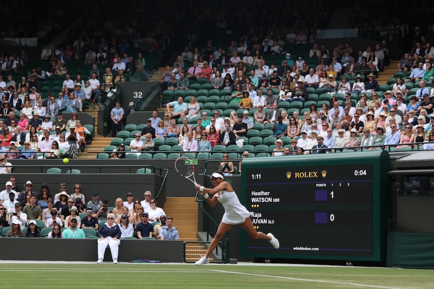 A tennis player in front of a crowd with several empty seats seen in Wimbledon stadium. 