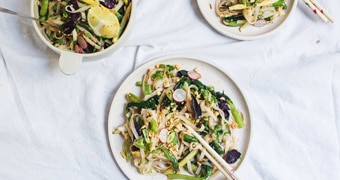 A bowl of pad thai salad with tongs served onto two dinner plates with chopsticks, illustrating our simple recipe.