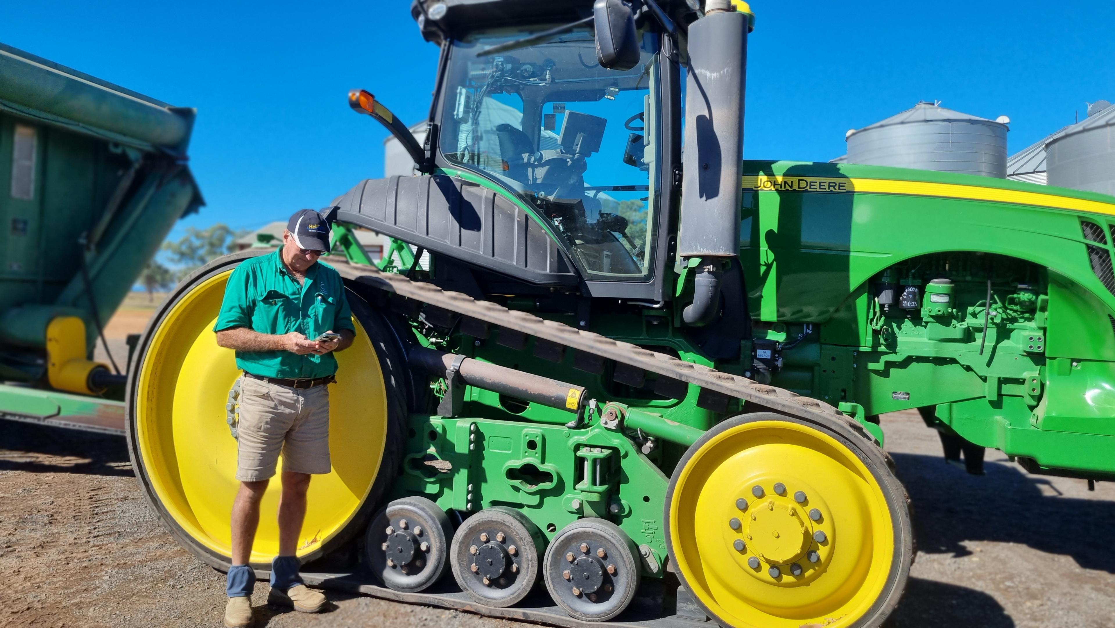 A man stands in front of a tractor and looks at his phone.