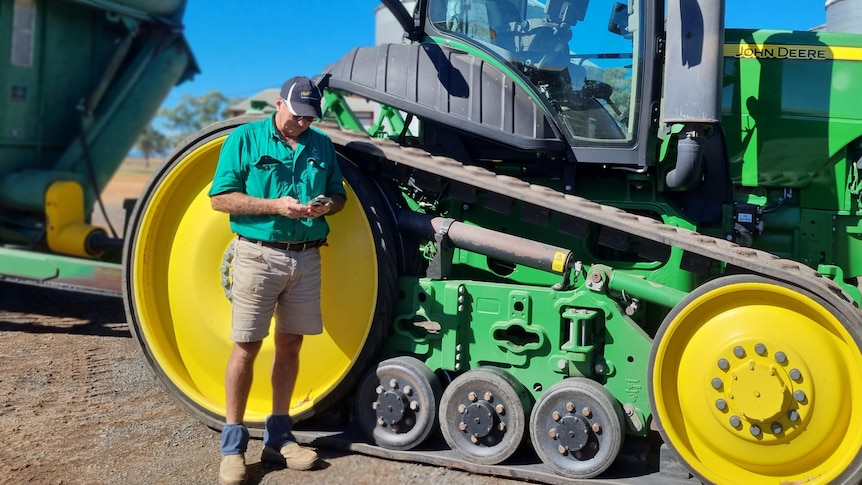 A man stands in front of a tractor and looks at his phone.