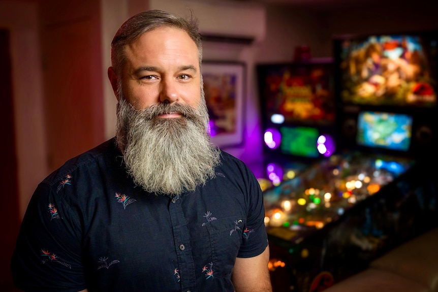 Michael Lloyd sitting in front of a pinball machine in his home