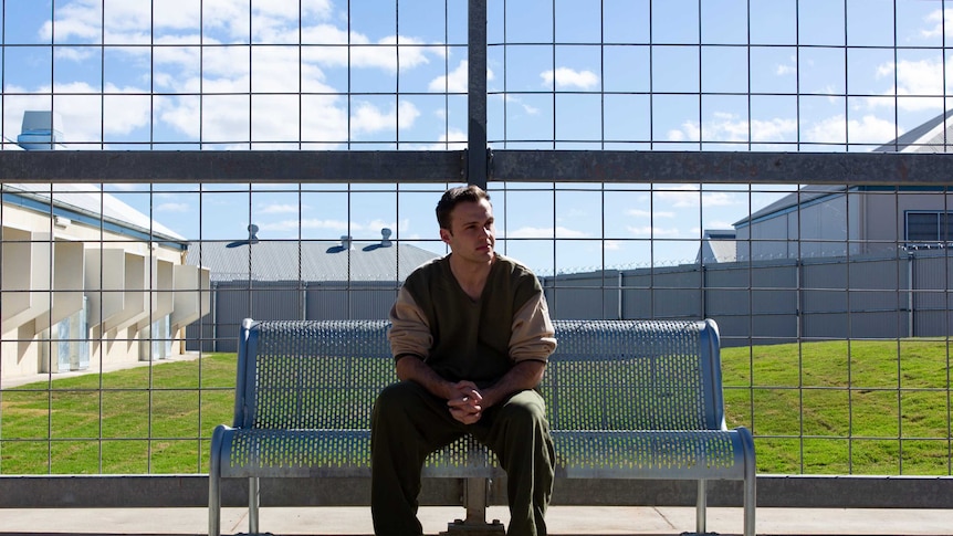 ABC reporter Tim Swanston sitting on a bench in a prison