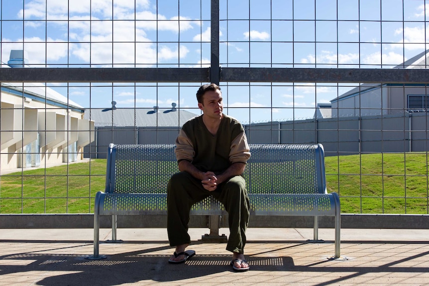 ABC reporter Tim Swanston sitting on a bench in a prison