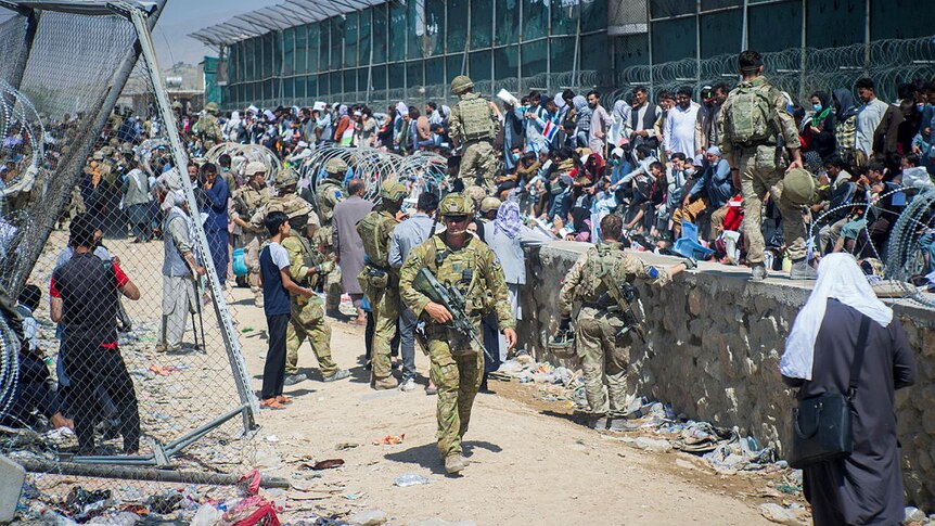 Soliders patrol as swathes of people congregate along a wall.