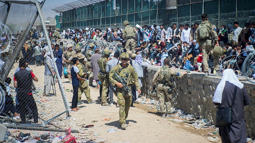 soliders in military uniform patrol as swathes of people congretate along a wall